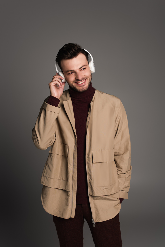 Smiling man in autumn outfit listening music in headphones isolated on grey  - Fotó, kép