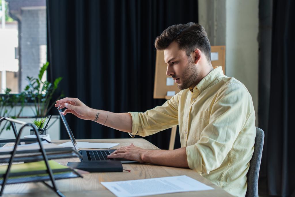 Вид збоку бізнесмена, використовуючи ноутбук біля документів на столі в офісі
  - Фото, зображення