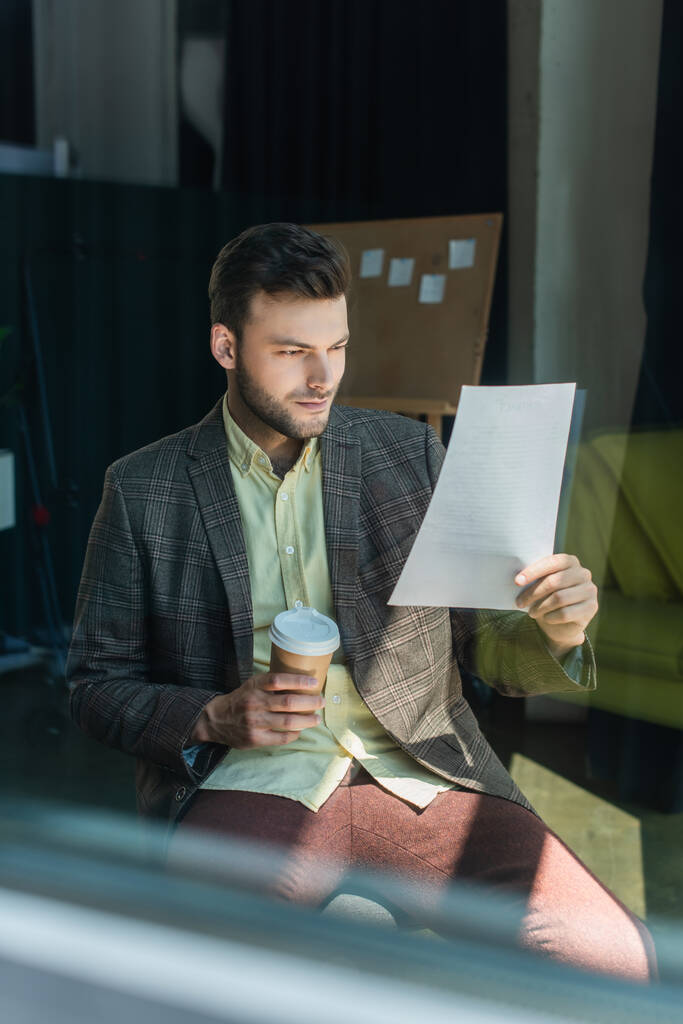 Бізнесмен дивиться на папір і тримає каву на винос в офісі
  - Фото, зображення