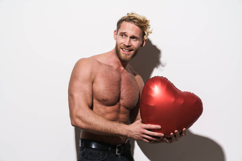 Shirtless blonde man smiling while posing with heart balloon isolated over white background - 写真・画像