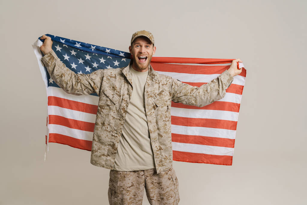 Valkoinen sotilas huutaa poseeratessaan Amerikan lippu eristettynä valkoisen muurin yli. - Valokuva, kuva