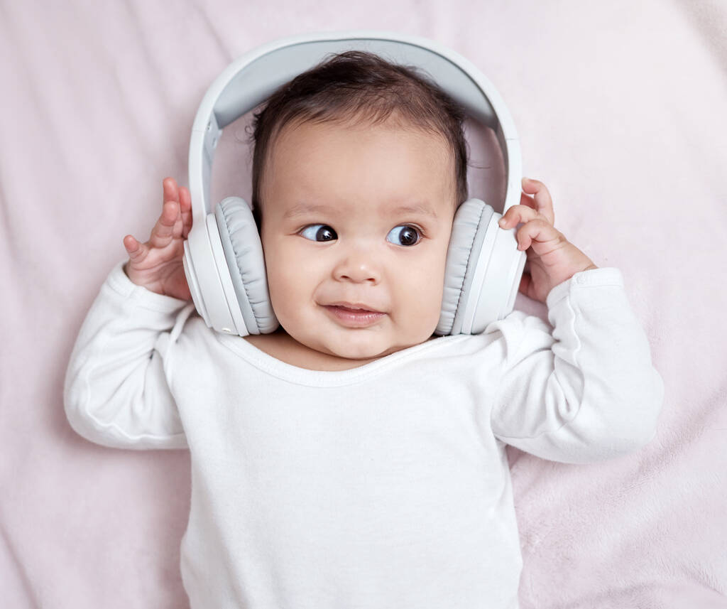 Hän stimuloi ja kehittää kuuloaistejaan. Korkea kulma laukaus ihana vauva yllään kuulokkeet kotona - Valokuva, kuva