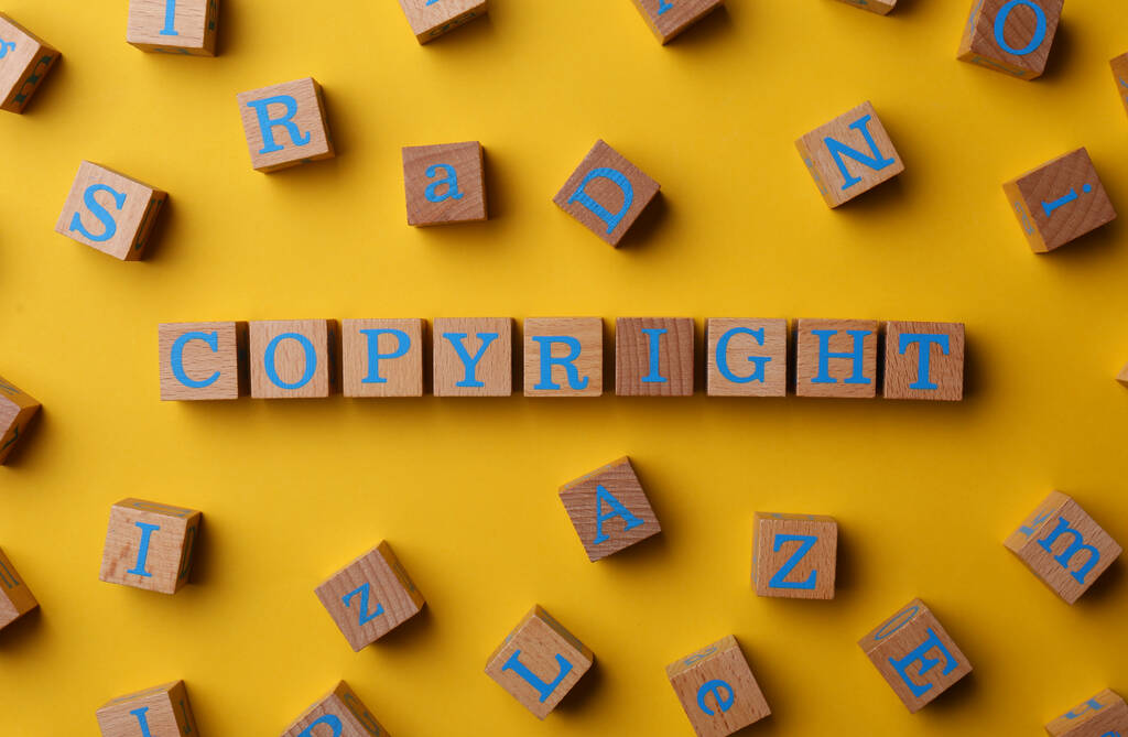 Plagiarism concept. Word Copyright made of wooden cubes on yellow background, top view - 写真・画像