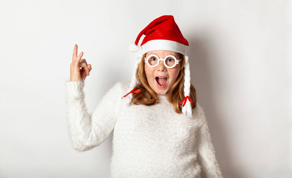 Children Christmas party, girl in santa hat shows rock and roll isolated on a white background. - Photo, image