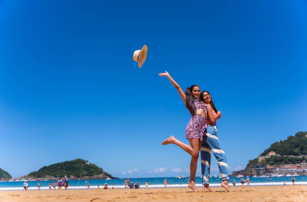 Two friends on summer vacation at the beach throwing a hat of joy, sea, lifestyle - Фото, изображение
