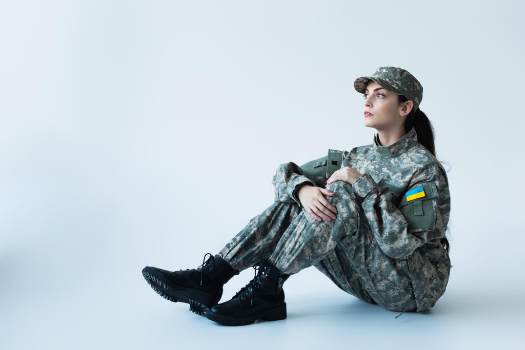 Soldier in military uniform with ukrainian flag sitting on grey background - Foto, imagen