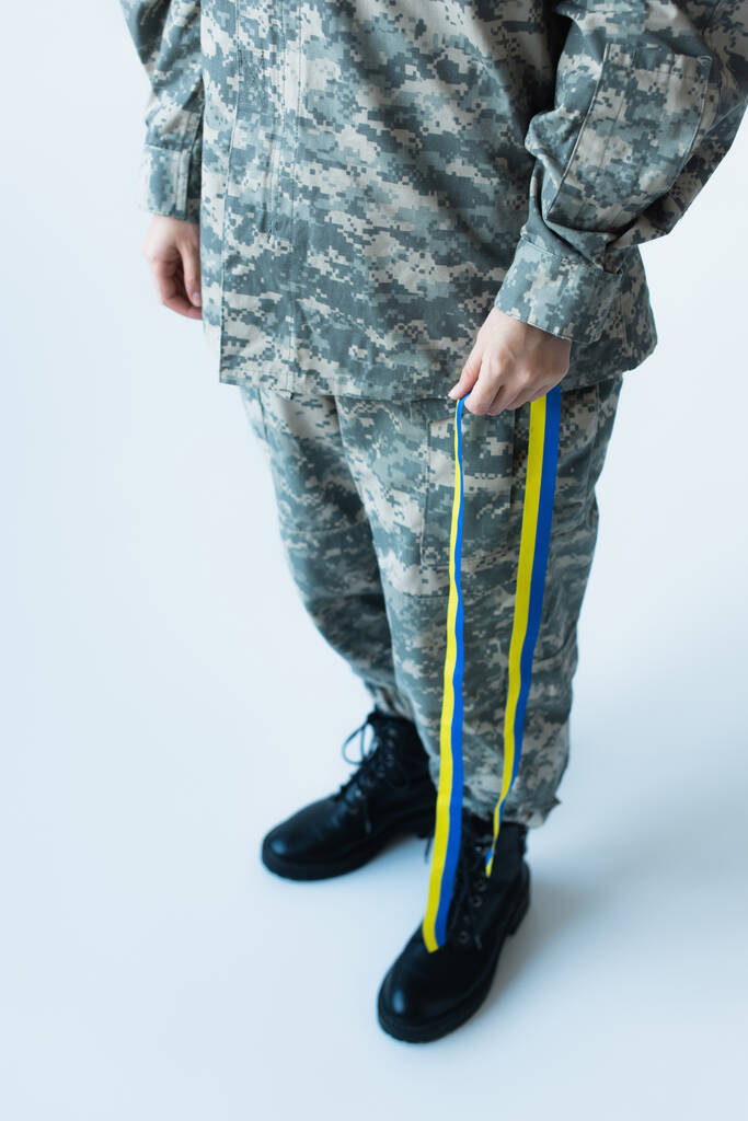 Cropped view of soldier holding blue and yellow ribbon on grey background - Φωτογραφία, εικόνα