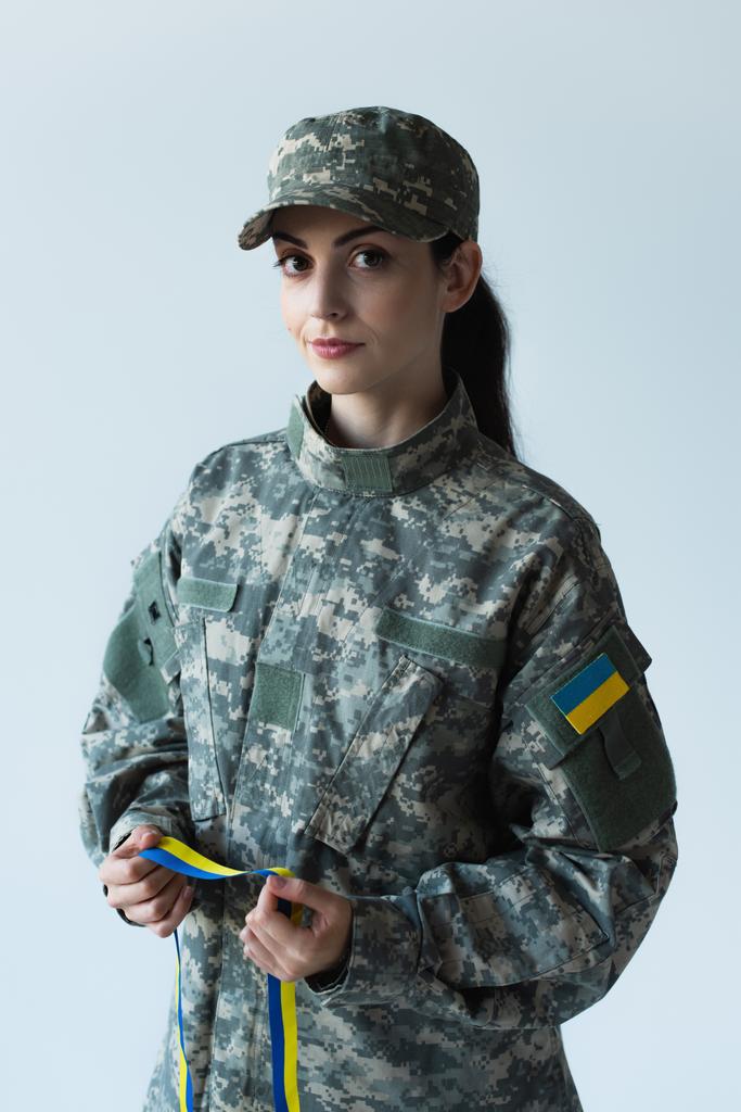 Soldier in cap and uniform holding blue and yellow ribbon isolated on grey  - Foto, Imagem