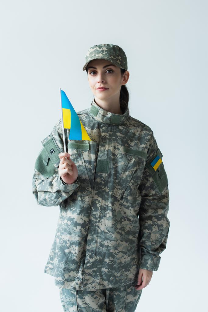 Fiatal katona kezében ukrán zászló és néz kamera elszigetelt szürke  - Fotó, kép