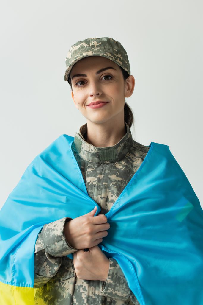 Portrait of smiling soldier covering with ukraining flag isolated on grey  - Foto, Imagen