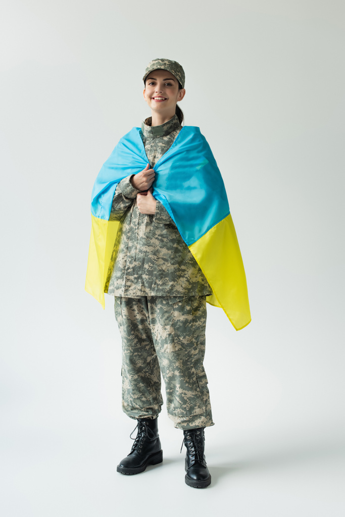 Gelukkig soldaat omhulsel met Oekraïense vlag op grijze achtergrond - Foto, afbeelding