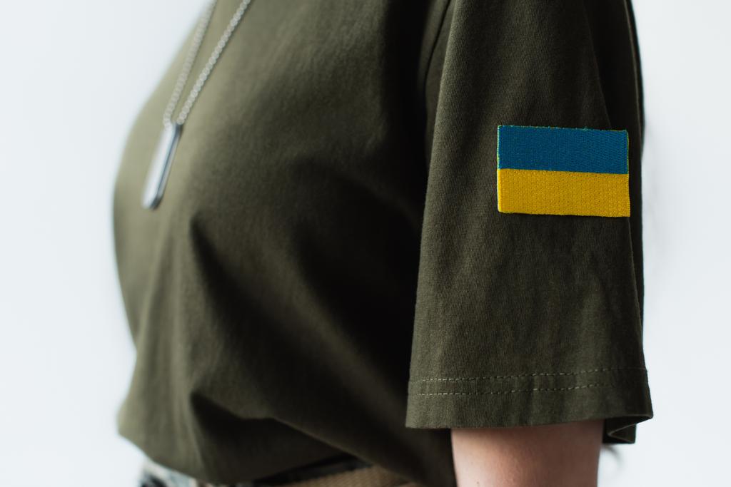 Cropped view of ukrainian flag on chevron of blurred soldier isolated on grey  - 写真・画像