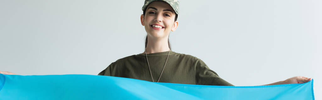 Wesoła służąca w mundurze trzymająca niebieską szmatkę na szarym, szarym transparencie  - Zdjęcie, obraz