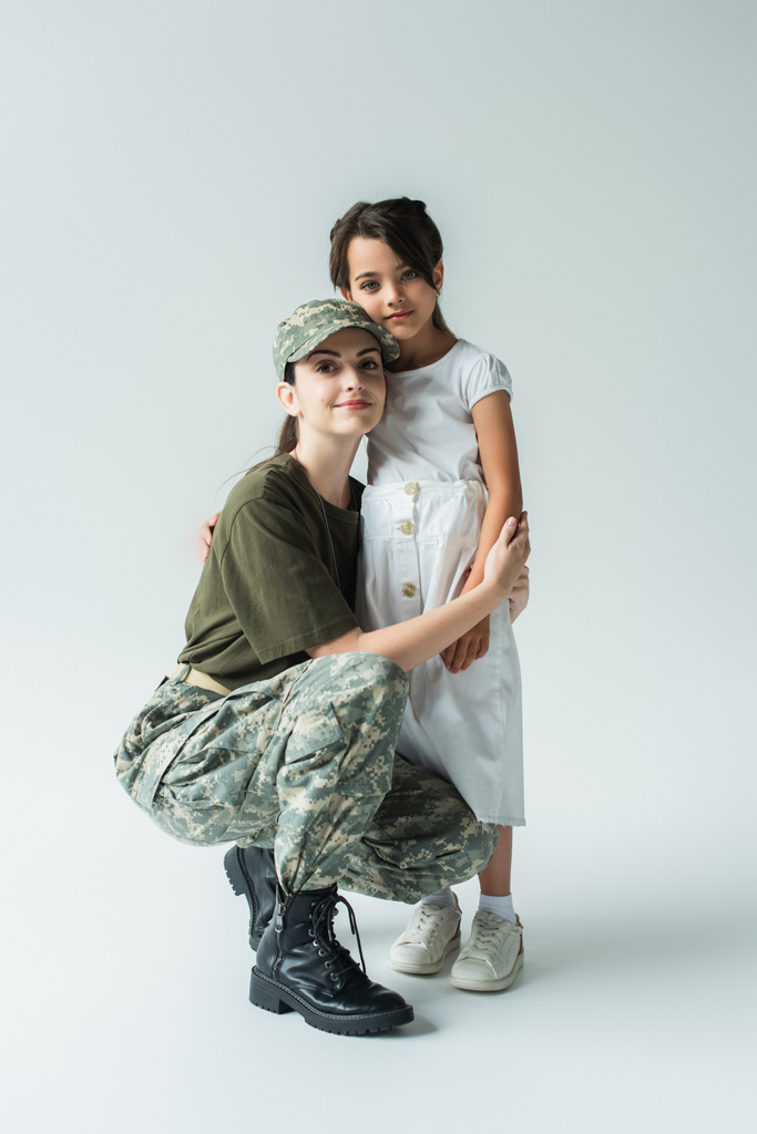 Young parent in military uniform hugging daughter on grey background - Foto, Imagen