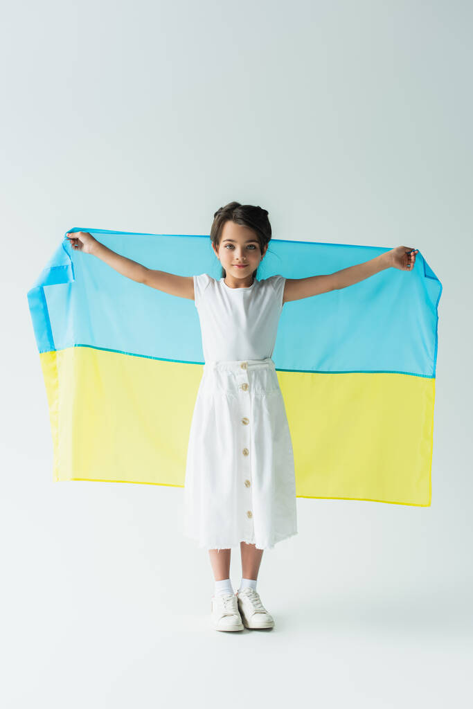 Kid holding ukrainian flag and looking at camera on grey background - Foto, immagini