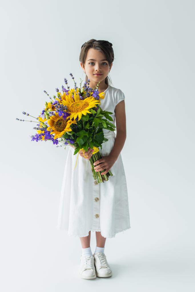 Full length of child holding blue and yellow bouquet on grey background - Φωτογραφία, εικόνα