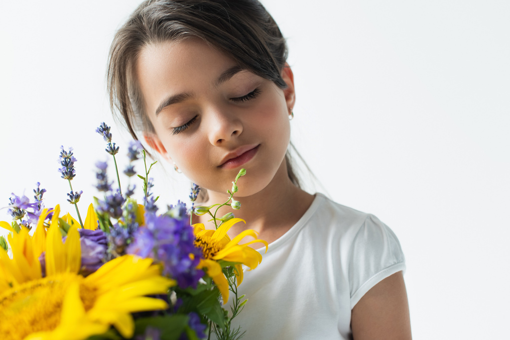 Portrait of kid closing eyes near blue and yellow flowers isolated on grey  - Zdjęcie, obraz