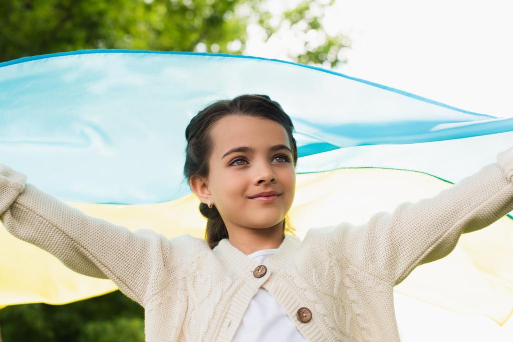 positive patriotic girl with ukrainian flag looking away outdoors - Fotografie, Obrázek