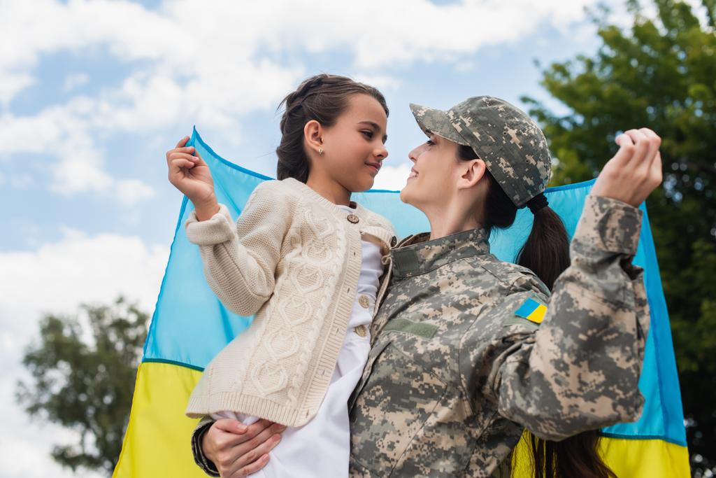girl and military woman with ukrainian flag smiling at each other outdoors - Zdjęcie, obraz