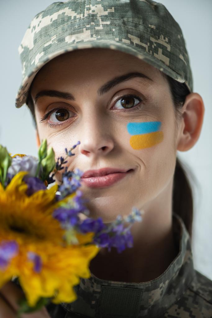 portrait of positive military woman looking at camera near flowers isolated on grey - Fotografie, Obrázek