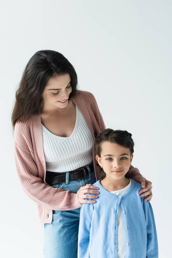 young brunette woman embracing daughter and smiling isolated on grey - Foto, afbeelding