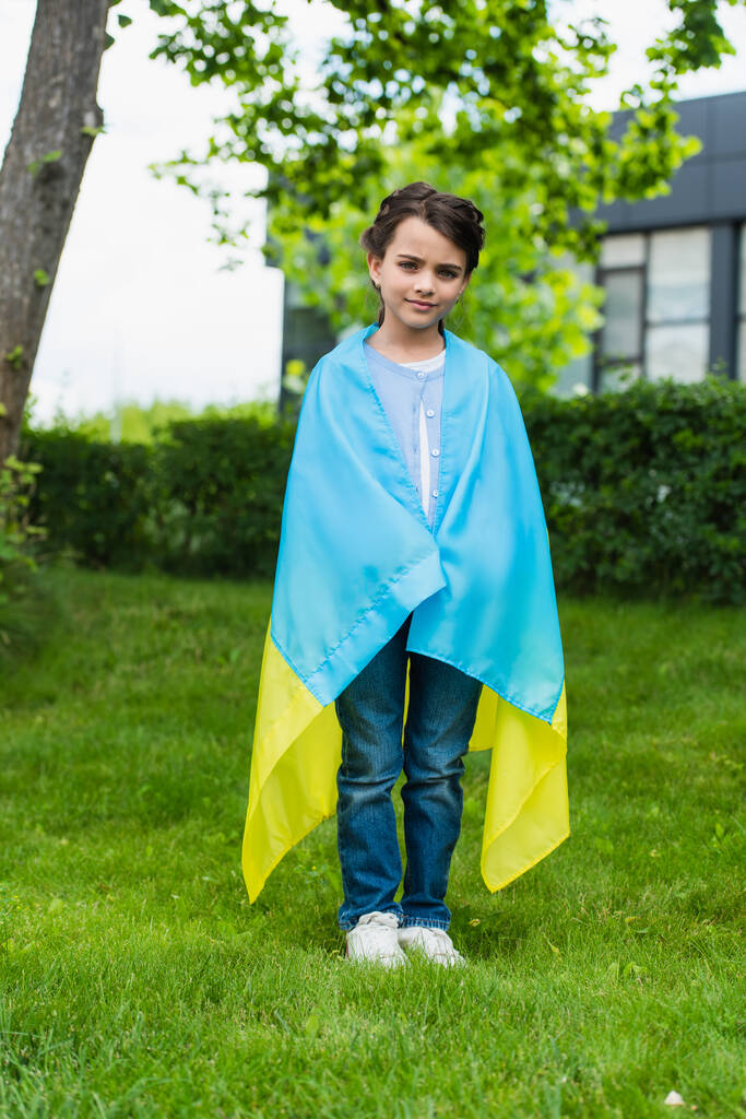full length of girl with ukrainian flag looking at camera in city park - Photo, image