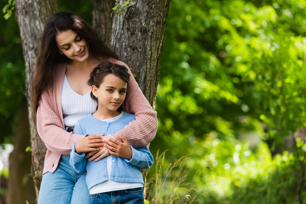 happy young woman hugging daughter near trees in park - Fotografie, Obrázek