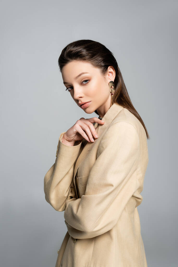 brunette young model in beige blazer looking at camera isolated on grey - Foto, afbeelding