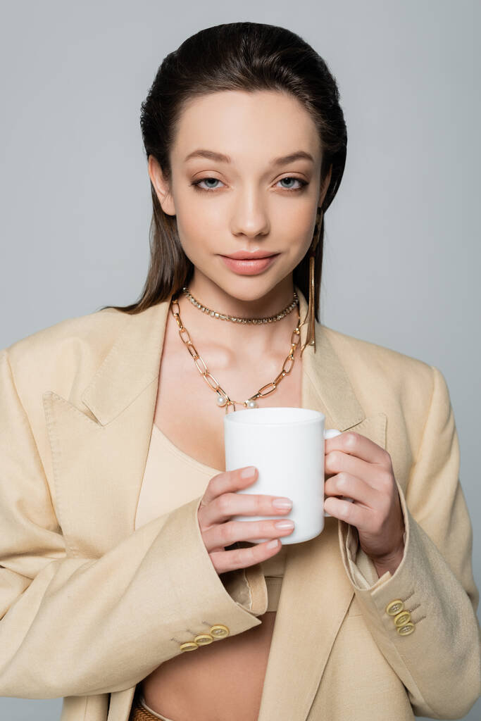 smiling woman in stylish beige suit holding cup of coffee isolated on grey - Foto, afbeelding