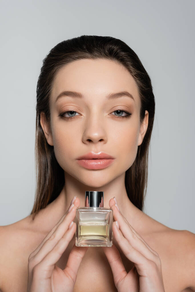 young woman with blue eyes holding bottle with luxury perfume isolated on grey - Fotografie, Obrázek