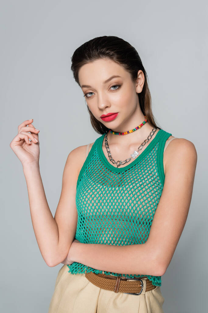 young and stylish woman with red lips and necklaces posing isolated on grey - Foto, immagini