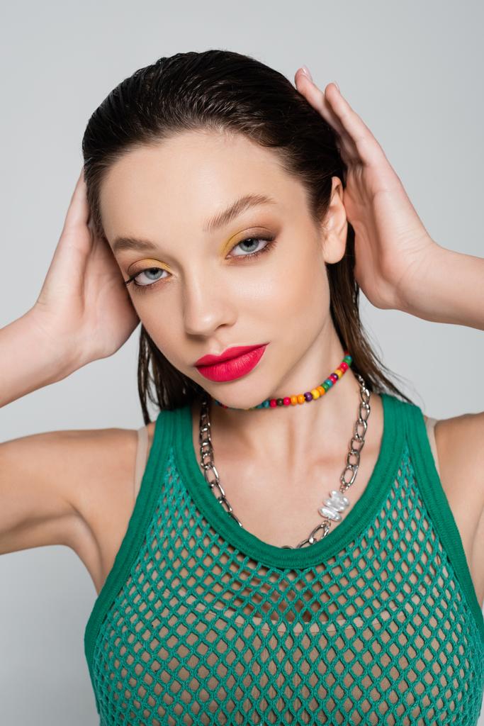 young brunette woman in trendy outfit with bright makeup isolated on grey - Foto, afbeelding