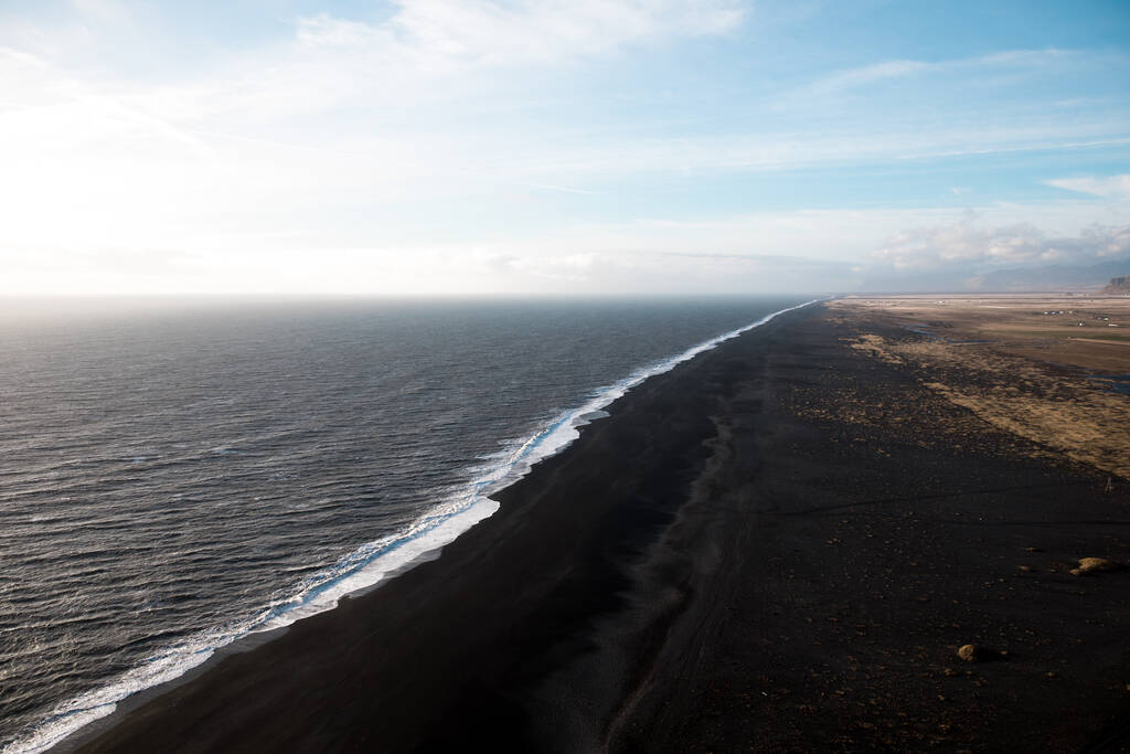 青い空の下でアイスランドの黒い砂の海岸線 - 写真・画像