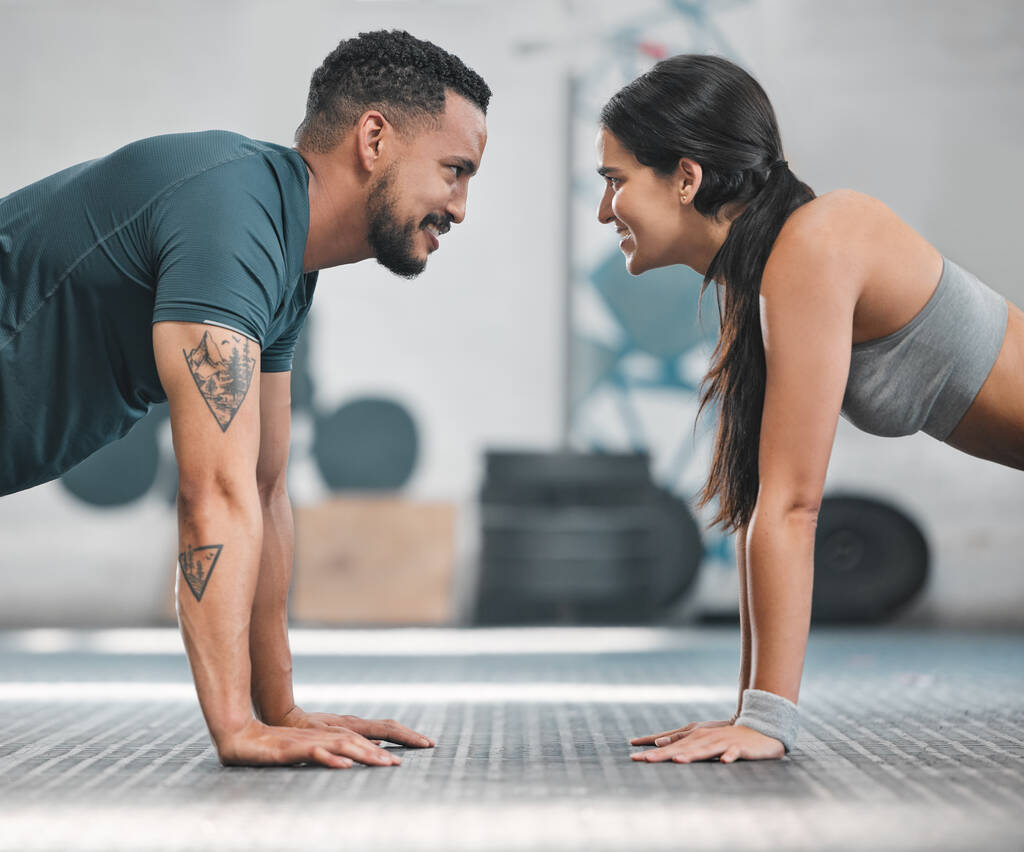 Fitness, health and active couple training together in a gym doing exercise workout for healthy lifestyle. Young and focused athletic friends doing pushups indoor. Good teamwork for wellness goals. - Fotó, kép