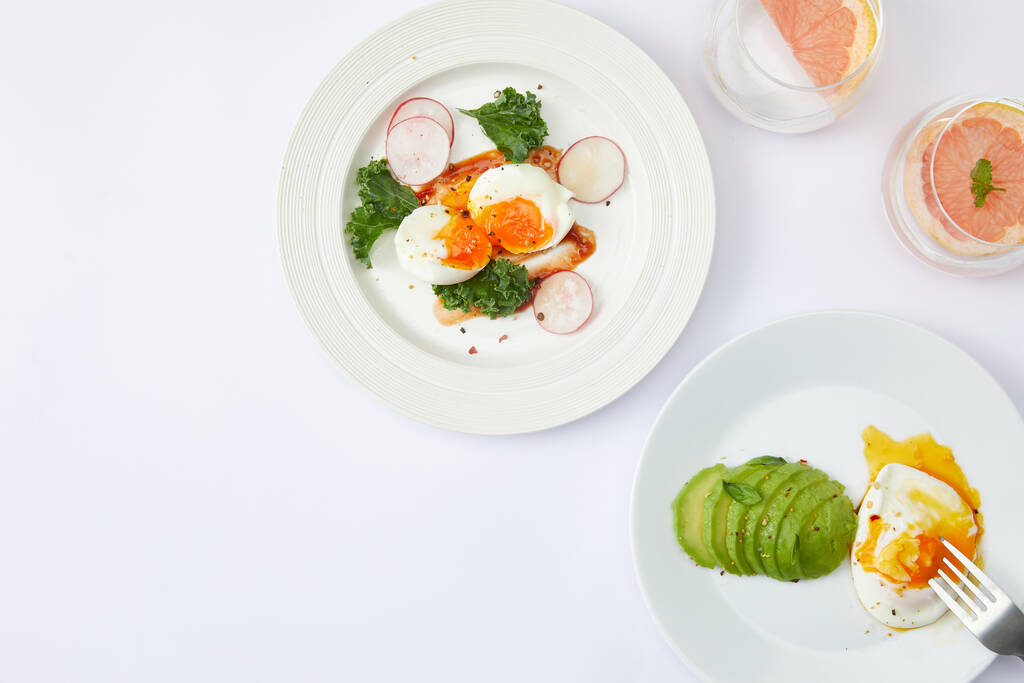 Een bovenaanzicht van gekookte eieren en avocado ontbijt maaltijden op een wit oppervlak - Foto, afbeelding