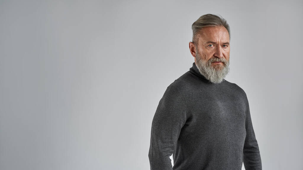 Senior confident caucasian man looking at camera. Stylish bearded pensioner wearing sweater. Concept of modern elderly male lifestyle. Isolated on grey background. Studio shoot. Copy space - Fotografie, Obrázek