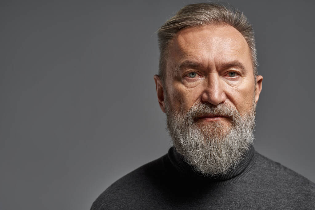 Portrait of serious senior caucasian man looking at camera. Stylish bearded pensioner wearing sweater. Concept of modern elderly male lifestyle. Isolated on grey background. Studio shoot. Copy space - Zdjęcie, obraz