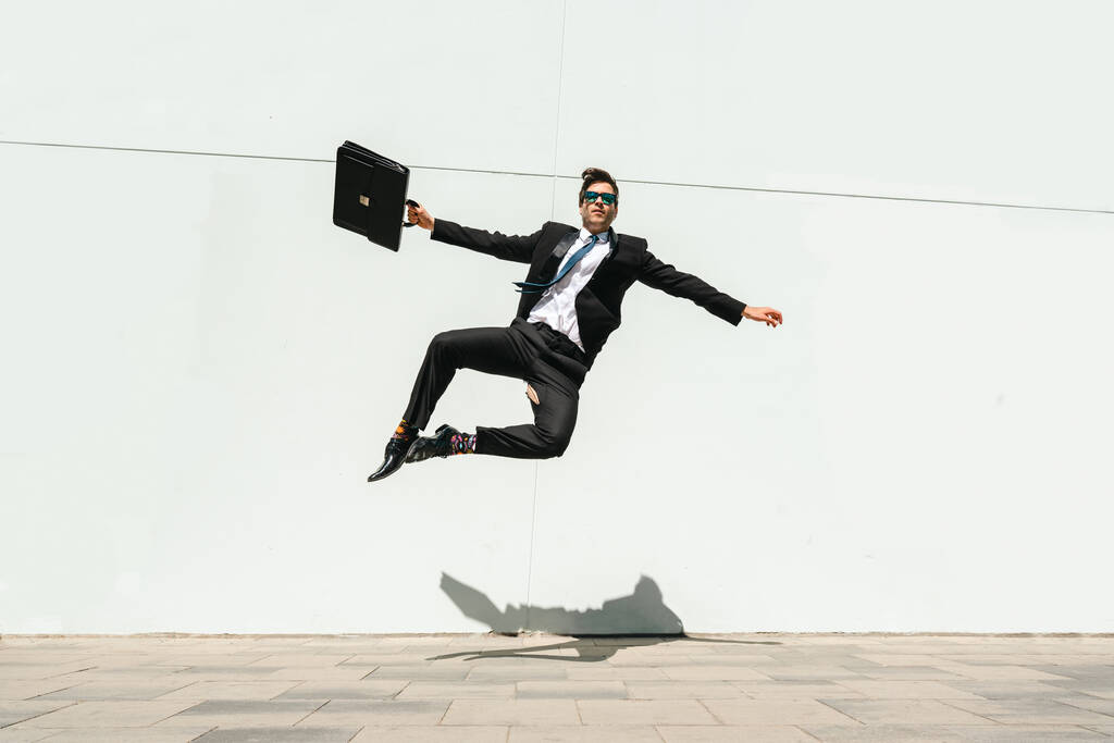 Happy and handsome adult businessman wearing elegant suit doing acrobatic trick moves in the city, alternative concept for business advertisement with energetic and creative people - Fotografie, Obrázek