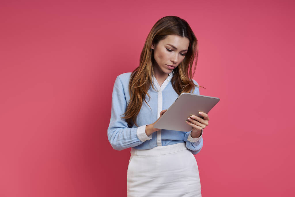 Confident young woman using digital tablet while standing against colored background - Fotoğraf, Görsel