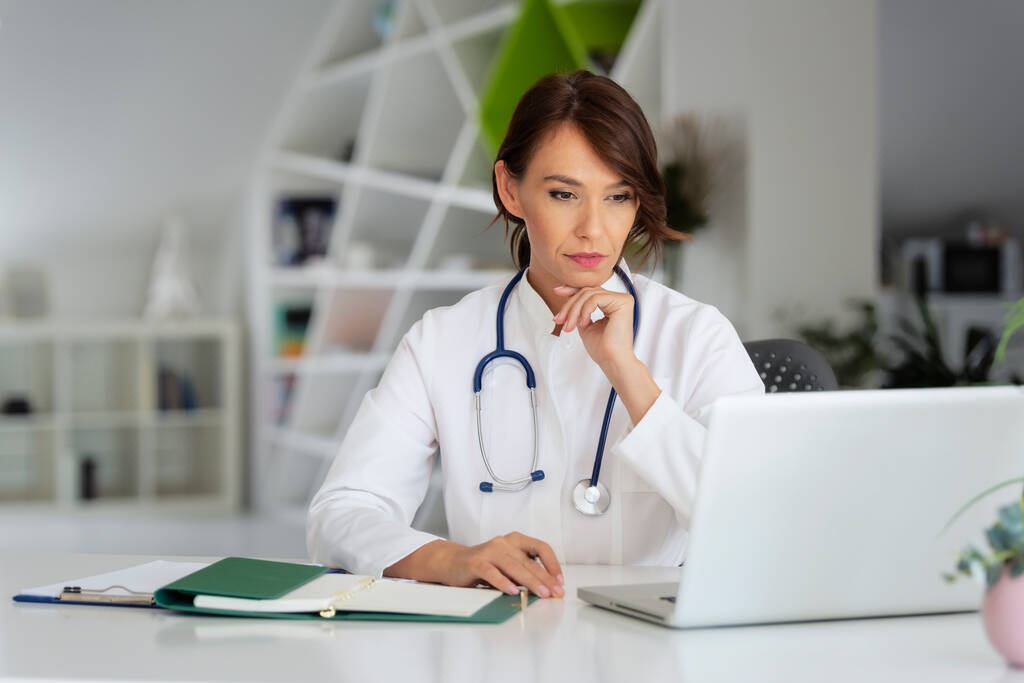 Shot of thinking femal doctor sitting behind a laptop  - Foto, immagini