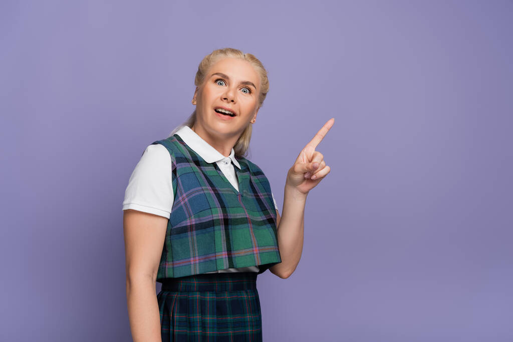 Amazed blonde student pointing with finger isolated on purple  - Foto, imagen