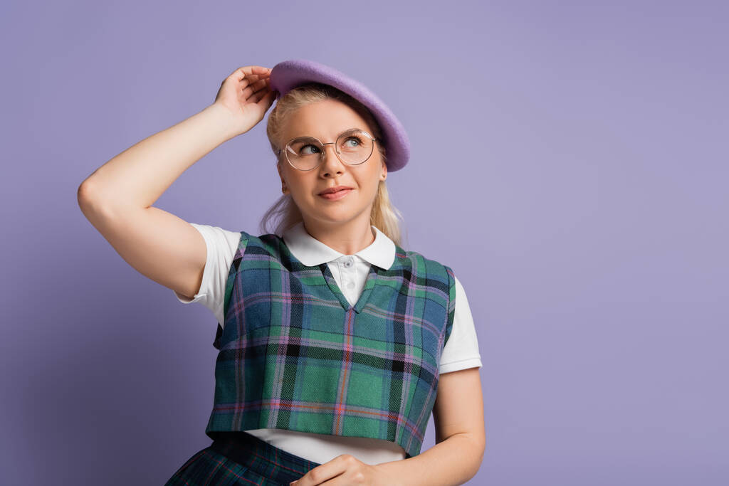 Blonde student in eyeglasses holding beret isolated on purple  - Foto, afbeelding