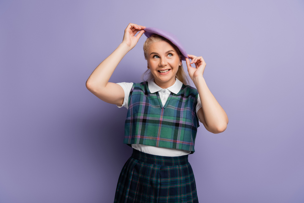 Smiling student in plaid uniform wearing beret on purple background  - 写真・画像