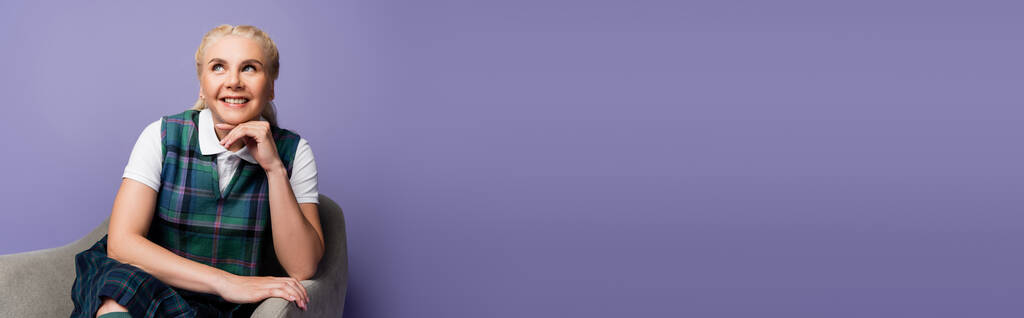 Positive student in plaid vest sitting on armchair isolated on purple, banner  - Fotoğraf, Görsel