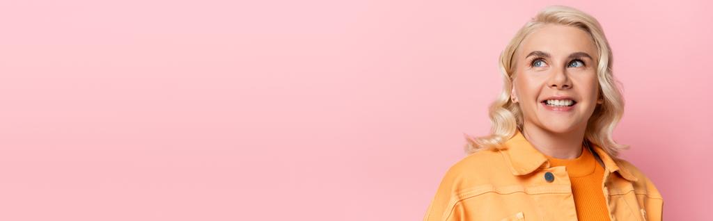 Positive blonde woman in jacket looking up isolated on pink, banner  - Zdjęcie, obraz