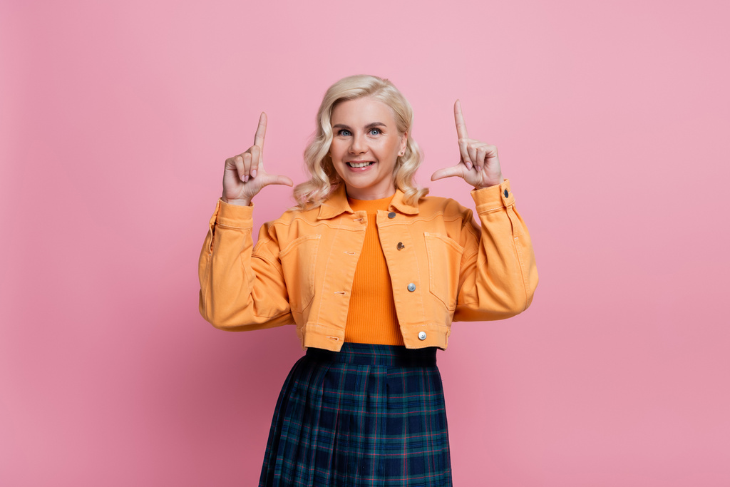 Smiling blonde woman looking at camera and pointing with fingers isolated on pink  - Foto, afbeelding