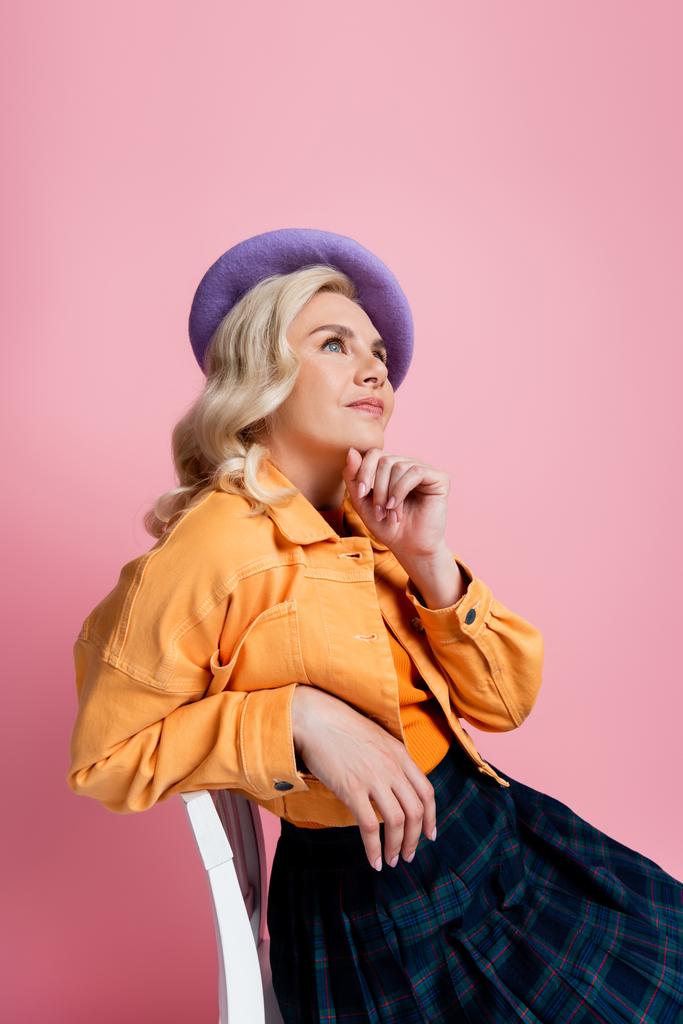 Dreamy woman in beret sitting on chair isolated on pink  - Fotografie, Obrázek