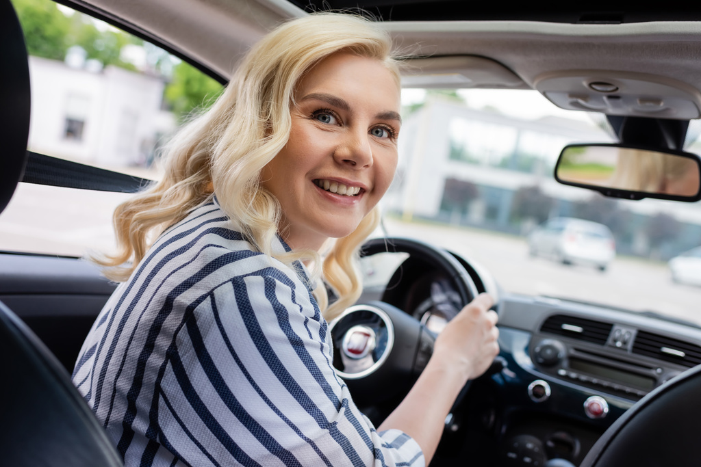 Позитивна блондинка дивиться на камеру під час керування автомобілем
  - Фото, зображення