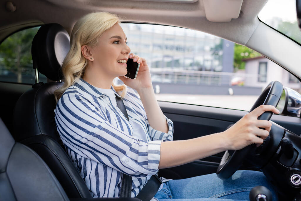 Side view of positive blonde woman talking on cellphone in car  - Valokuva, kuva