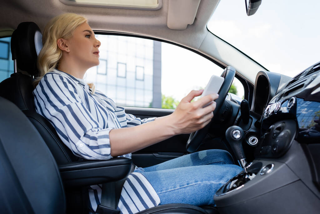 Side view of woman using smartphone and driving car  - Foto, Imagem